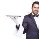 Smiling waiter holding an empty silver tray, isolated on white background