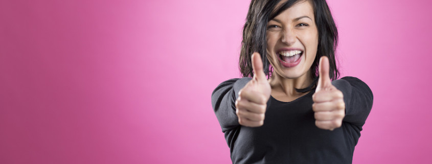 Excited, happy girl giving thumbs up showing success, isolated on pink background.