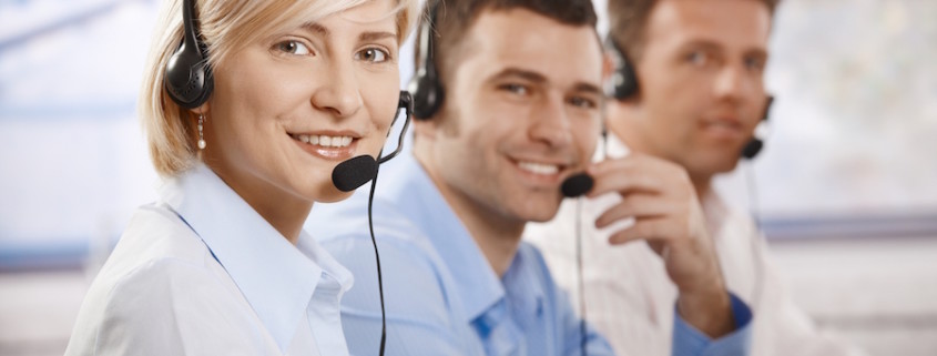 Happy young customer service operators talking on headset, looking at camera, smiling.